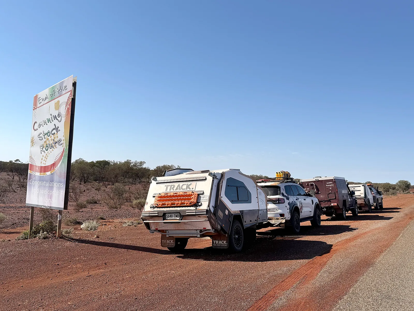 A convoy of four-wheel drives and off-road campers beside the End of the Canning Stock Route sign welcoming travellers to Wiluna