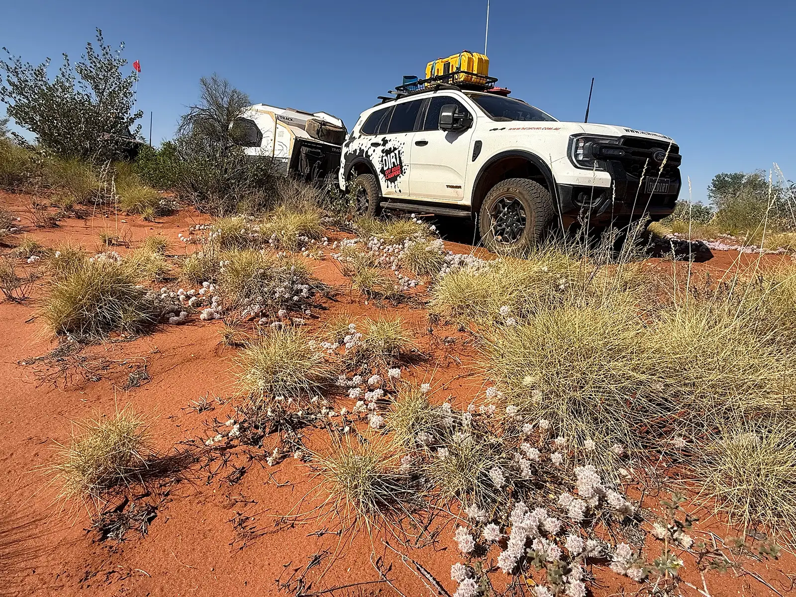 Ford Everest Tremor towing a Track Trailer Mk6 Tvan along a red dirt track through spinifex, with a sand flag flying