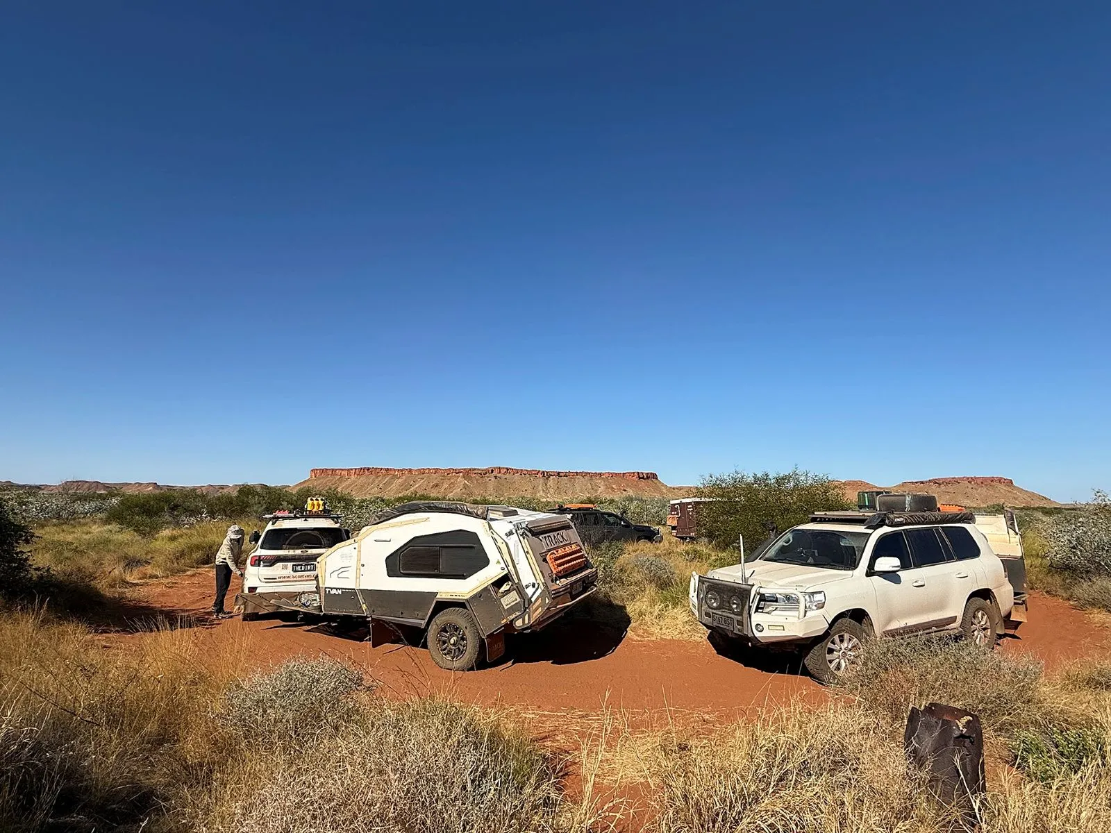 Track Trailer Mk6 Tvan stopped with two four-wheel drives on a red dirt track beneath a red desert escarpment