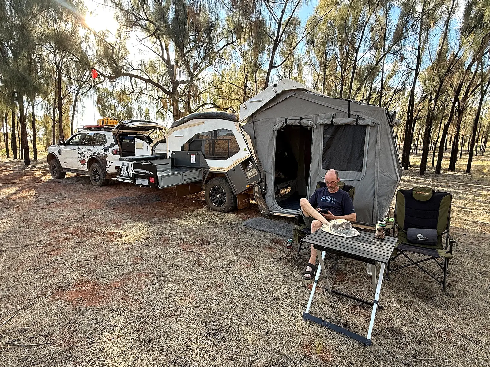 Track Trailer Mk6 Tvan set up beneath the trees beside a Ford Everest, with the kitchen and living area open