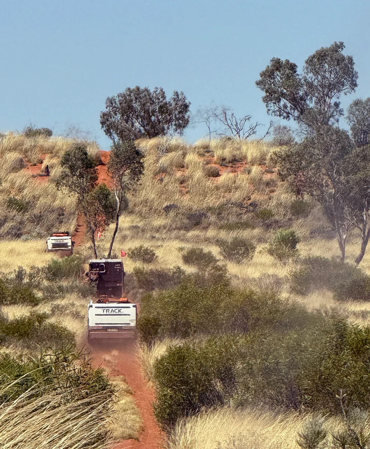 Track Trailer Tvan following another vehicle along a narrow dusty red track through tall grass and scrub